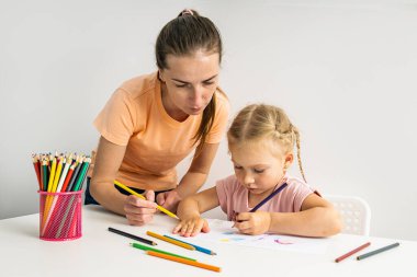 Teacher helps child girl draw together with colored pencils on paper.