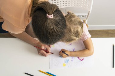 Child girl with mom draw with colored pencils on white paper. Top view, flat lay.