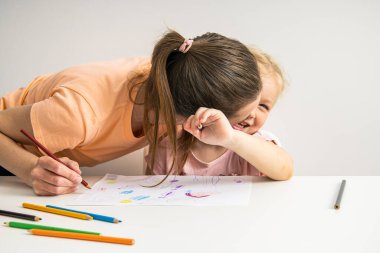 Joyful hugging mom and child girl draw together with colored pencils on paper.