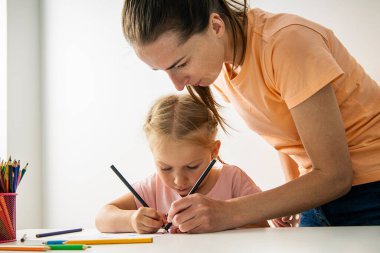 Child girl with mom draw with colored pencils on white paper.