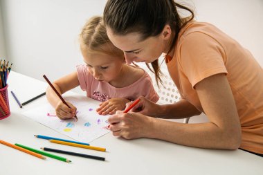 Child girl with mom draw with colored pencils on white paper.