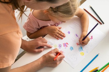 Child girl with mom draw with colored pencils on white paper. Top view, flat lay.