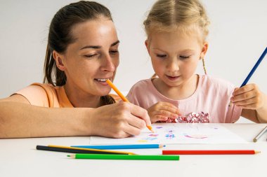 Joyful mother and daughter drawing together with colored pencils on paper.