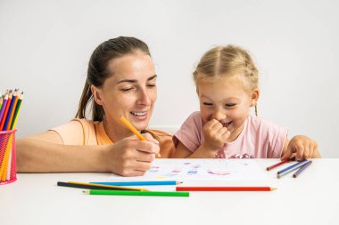 Joyful mother and daughter drawing together with colored pencils on paper.