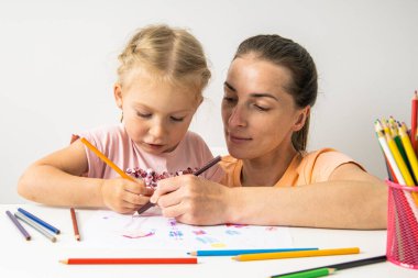 Child girl with mom draw with colored pencils on white paper.