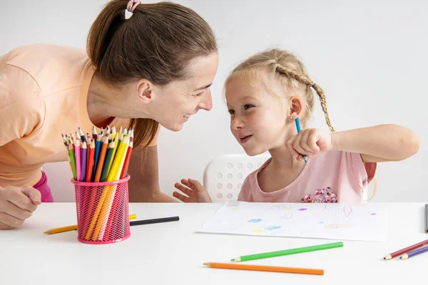 Blonde child girl draws with colored pencils sitting at the table. Top view, flat lay.