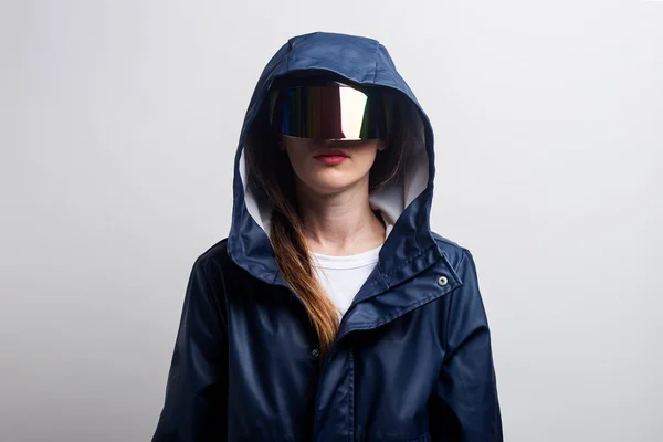 Young woman of the future in virtual reality glasses, in a blue jacket on a light background.