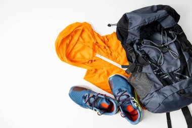 Turist çantası, yağmurluk, beyaz arka planda spor ayakkabılar. Üst manzara, düz uzanma.