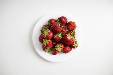 Beyaz masa arkasında çilekli beyaz tabak. Üst manzara, düz uzanma.