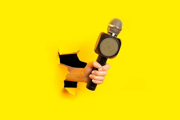 Mão Mulher Segura Microfone Buraco Fundo Amarelo Brilhante Rasgado — Fotografia de Stock