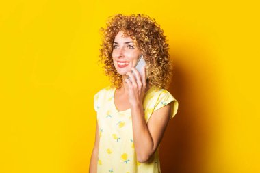 Sarı arka planda telefonla konuşan, gülümseyen kıvırcık bir genç kadın.