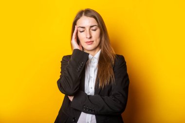 Kapalı gözlü yorgun genç bir kadın sarı arka planda şakağına bir avuç dolusu tutar..