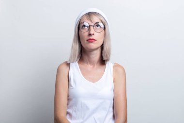 Gözlüklü sarışın genç bir kadın, beyaz şapkalı bir kadın açık arkaplanda yukarı bakıyor..