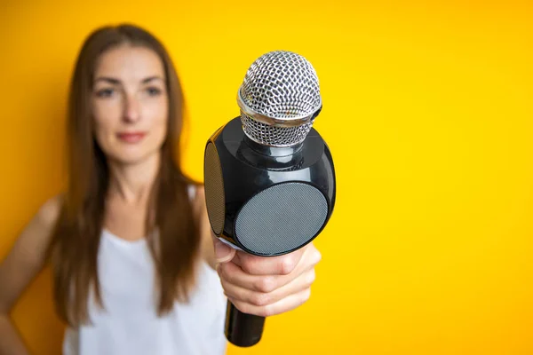 Young woman holding a microphone, interviewing on a yellow background. Reporter or journalist concept.