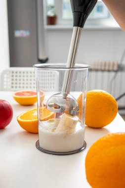 Kadın elleri mutfakta taze meyve karıştırmak için el blenderi kullanır..