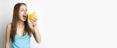 Beyaz arka planda taze sarı biber yiyen genç bir kadın. Pankart.