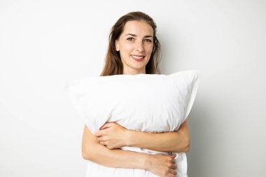 Beyaz arka planda beyaz yastığı tutan gülümseyen genç kadın..