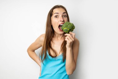 Beyaz arka planda taze yeşil brokoli yiyen genç bir kadın..