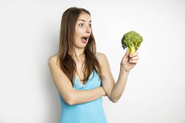 Beyaz arka planda taze brokoli görünce şaşıran genç bir kadın..
