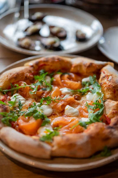 レストランのテーブルの上にルコラとサーモンの美味しいイタリアンピザ — ストック写真