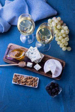Mavi peynirli aperatifin üst görüntüsü ve ahşap bir tahtanın üzerinde bal, üzüm ve mavi arka planda bir bardak şarapla peynirli camembert.