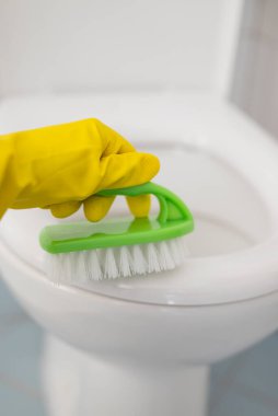 Eldivenli bir kız, eldivenli klozet kapağını fırçayla yıkıyor.