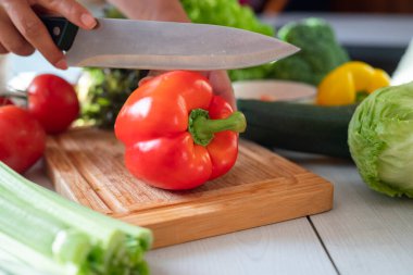 Mutfakta aşçı kız kırmızı biber ve sebze kesiyor.