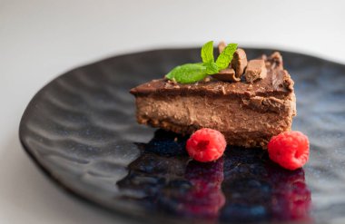 delicious sweet chocolate cheesecake cake in a restaurant with raspberries and mint leaf on a plate