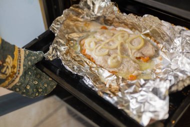 Bir kadın aşçı fırından fırından bir tabak balık çıkarır.