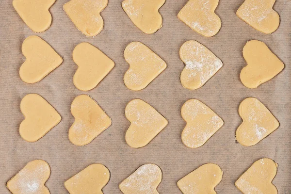 Shortbread homemade cookies in the shape of a heart are laid out in rows on parchment. Close-up. Cooking recipe. Top view