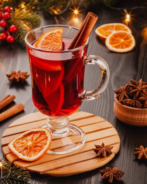 Bir bardak tarçın çubuklu sıcak şarap ve şenlikli bir arka planda portakal dilimleri. Noel atmosferi, yeni yıl. Yıldız anason, çelenk, arka planda köknar dalları. Kafe reklamı. Dikey fotoğraf.