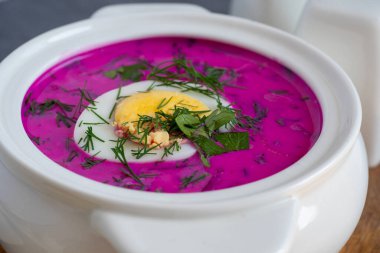 Ahşap bir tahtanın üzerinde soğuk chlodnik çorbası. Yarım yumurtayla süslenmiş, pancar kökü ve kefirden yapılmış Polonya usulü Belarus ve Rus mutfağı çorbası. Sağlıklı yemek.