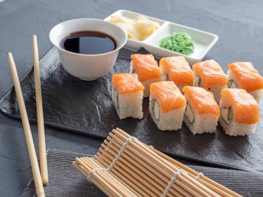 Suşi Philadelphia 'yı gri arka planda siyah desenli bir tabakta yuvarlıyor. Wasabi zencefili ve sos çubukları. Somon, krem peynir, avokado..