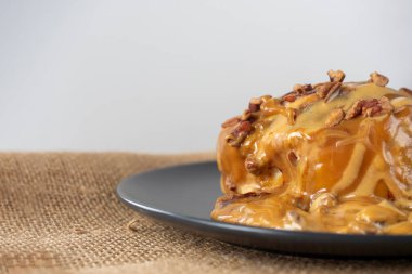 Karamel soslu ve cevizli tarçınlı çöreğin yakın çekimi. Siyah plaka, yan görüş. Lezzetli tatlı, bulanık arkaplan. Seçici odak, boşluğu kopyala