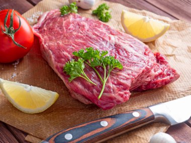 Baharatlar, otlar ve sebzelerle çevrili bir parça taze çiğ et parşömenin üzerinde yatıyor. Bıçak yakınlarda yatıyor. Yan görüş. Yiyecek bileşimi