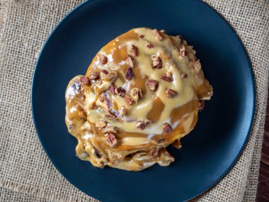 Karamel soslu ve cevizli tarçınlı çöreğin yakın çekimi. Siyah tabak, keten peçete. Üst manzara, düz uzanma