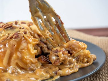 Karamel serpilmiş ve fındıkla süslenmiş tarçınlı çöreğin yakın çekimi siyah bir tabakta ve keten peçetede yatıyor. Yan manzara, bir parça tatlı çatalla alınır. Seçici odak