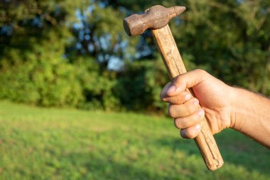 Eski, kirli bir çekiç tutan bir adamın yakın çekimi. Bulanık yeşil arka plan. Boşluğu kopyala