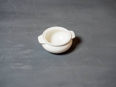 Beyaz porselenden yapılmış boş bir tencerenin, dokusu gri bir arka planda durduğu yakın plan. Yemek için tabaklar