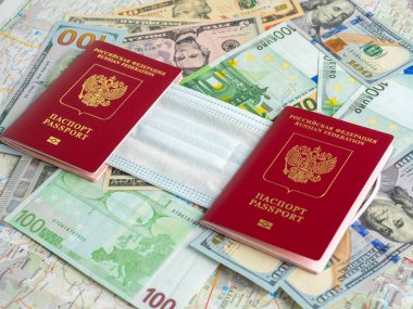 Dolar ve avro banknotlarında iki Rus pasaportu var. Pasaportların arasına tıbbi maske takılmış. Salgın ve hastalıklar sırasında seyahat etme kavramı