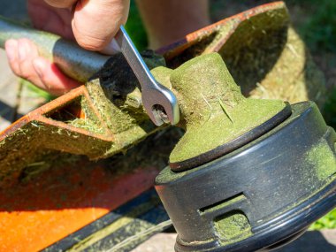 Çim biçme makinesinin yakın plan çekiminde vites kutusundaki vida İngiliz anahtarıyla sökülmüş. Ekipmanların bakımı, vites kutusunun yağlanması.