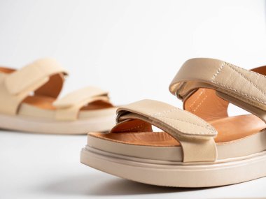 Beyaz arka planda bej deri sandaletler. Bir çift ayakkabı, kadın uçuş ayakkabısı.