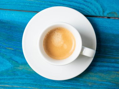 Mavi ahşap zemin üzerinde taze demlenmiş espresso ile beyaz bardak. Üst manzara, düz yatış, kahverengi köpük. Kahve konsepti