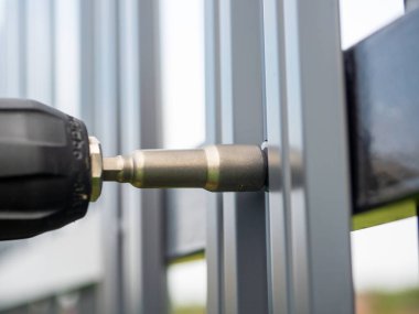 Çatı vidalarını metal çitlere vidalamaya yakın plan. Çit kuruluyor.