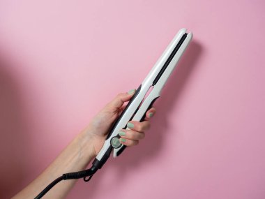 Beyaz saç maşası arka planda bir kadının elinde. Saç stili yaratmak için bir aksesuar. Güzellik ve moda. Saç bakımı.