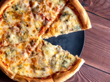 Kahverengi ahşap arka planda dört peynirli hazır İtalyan pizzasının yakın çekimi. Üst manzara, düz yatış. Geleneksel bir İtalyan yemeği. Ev yemeği. Dilimlerden biri yenmiş.