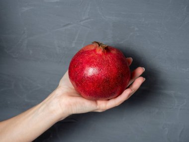 Bir kadının eli, gri arka planda olgun sulu bir nar meyvesi tutar. Sağlıklı ve lezzetli meyveler..