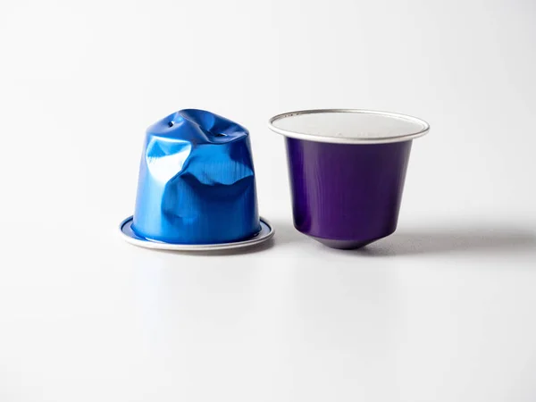 两个蓝色和紫色铝胶囊 底色为白色咖啡 其中之一被使用 材料储存和加工的概念 环保产品 — 图库照片