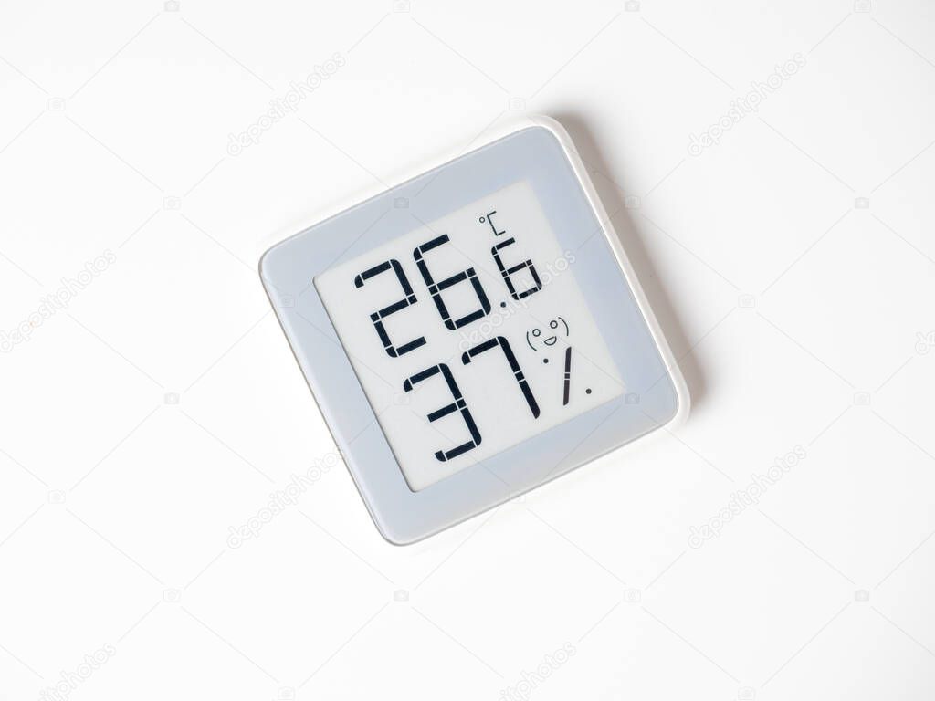 A home weather station standing on a white background is a modern device with a screen showing the temperature and humidity in the room. Top view, flat lay