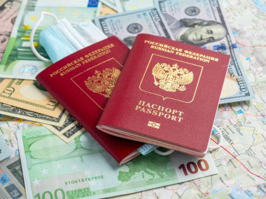 Dolar ve avro banknotlarında iki Rus pasaportu var. Pasaportlardan birine tıbbi maske takılmış. Salgın ve hastalıklar sırasında seyahat etme kavramı.